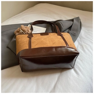 Detail of brown tote bag featuring embossed cat patterns and polished metal logo plate