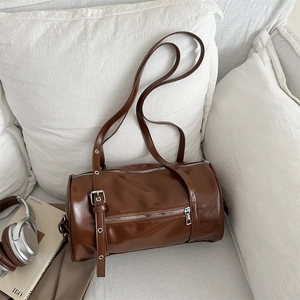 Chic brown cylindrical shoulder bag in glossy leather with silver hardware on a sofa