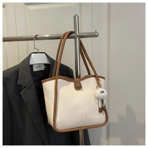 Detail of cream tote bag with brown trim featuring a cute plush doll charm