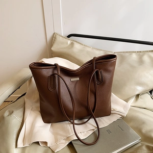 Brown lychee leather tote bag with metal plaque on an elegant minimalist white blazer background