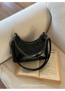 Detail of a black glossy leather shoulder bag with a chain strap on vintage books