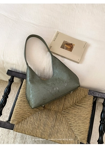 Detail of dark green crescent bag with vertical texture resting on a woven chair