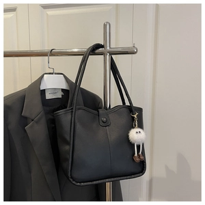 Detail of minimalist black matte leather tote bag with white plush eye charm accessory