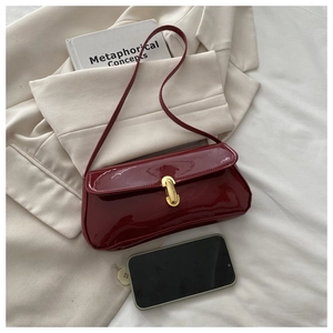 Close-up of wine red patent leather shoulder bag with golden metal clasp and glossy finish