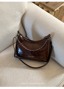 Close-up of a dark brown glossy leather bucket bag with silver chain on a beige sofa