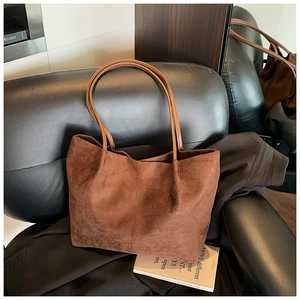 Detail view of brown faux suede tote bag with leather straps on a dark leather sofa