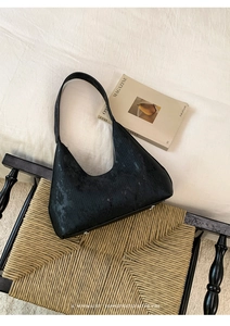 Detailed texture of black corduroy hobo bag with silver studs on a woven chair