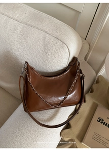 Detail of caramel brown moon bag with silver chain and glossy PU leather texture