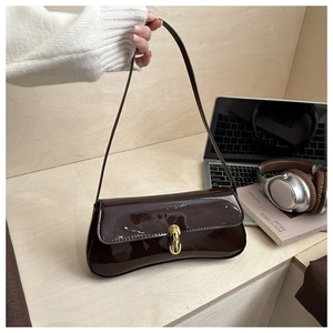 Detailed view of dark brown patent leather baguette bag with oval gold buckle and strap