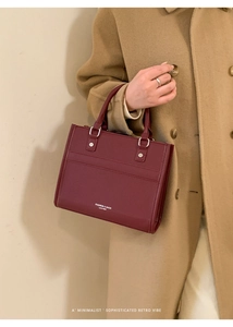 Elegante borsa tote in pelle bordeaux con scritte bianche tenuta da una modella in cappotto