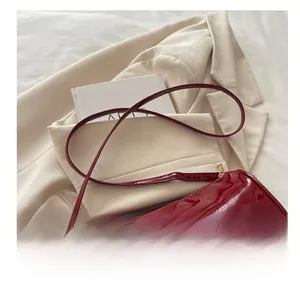 Détail du sac polochon en cuir verni rouge avec logo en métal sur blazer blanc