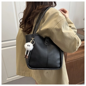 Detail of black tote bag with matte texture and cute monster plush charm on shoulder strap