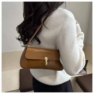 Detail of caramel brown glossy patent leather shoulder bag with golden metallic clasp