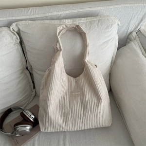 Grand sac cabas crème à texture plissée et large bandoulière posé sur un canapé