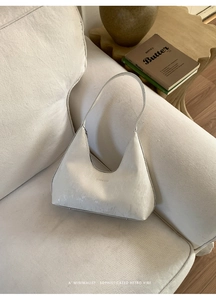 Detail of a creamy white hobo bag on a sofa featuring minimalist leather texture