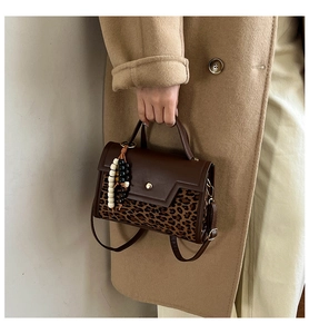 Close-up of brown leather handbag with leopard print panel and beaded charm detail