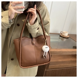 Brown leather tote bag detail with white plush doll charm accessory in home setting