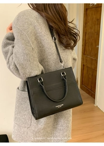 Dettaglio di una borsa tote in pelle nera indossata con un cappotto di lana grigia