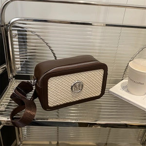 Retro brown leather camera bag with woven panels and wide shoulder strap on a shelf