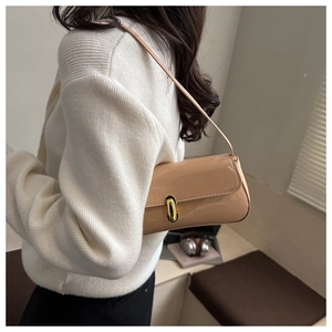 Model wearing a stylish beige patent leather baguette bag with a gold buckle clasp detail