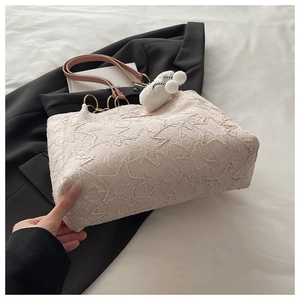 Detail of cream jacquard tote bag featuring floral texture and soft plush charm
