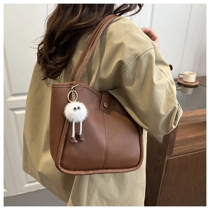 Brown leather tote bag with fluffy cartoon charm shown on model in beige trench coat