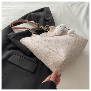 Detail of a cream tote bag with wrinkled texture, pink handles, and cloud plush charm