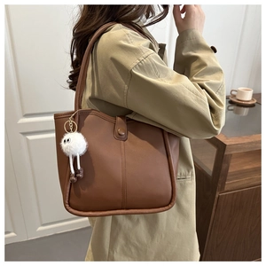 Brown leather tote bag featuring a cute white plush doll pendant on a shoulder strap