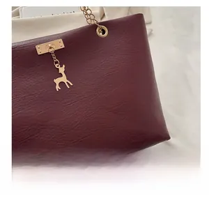 Gros plan d'un sac sous le bras bordeaux motif litchi avec breloque cerf doré et chaîne