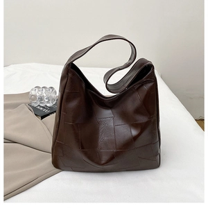 Detail view of dark brown patchwork leather tote bag on minimalist white bedding decor