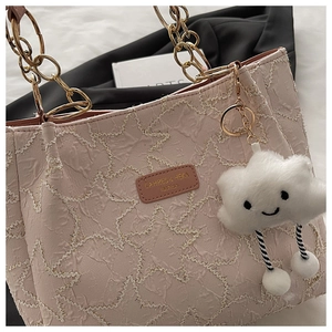 Detail of pink tote bag with star pleats, gold chain, and cute plush cloud charm