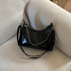 Chic black patent leather dumpling bag with silver chain on a soft textured sofa
