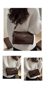 Detail of dark brown cylindrical crossbody bag with glossy finish and gold fashion logo