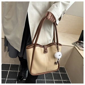 Close-up of retro beige tote bag with brown contrast trim and plush cartoon charm