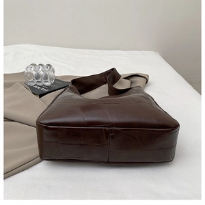 Detailed view of dark brown stitched hobo bag on white bedding with minimalist decor