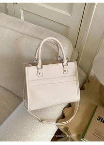 Close-up of off-white lychee leather tote bag with FASHION & BAGS logo on a sofa