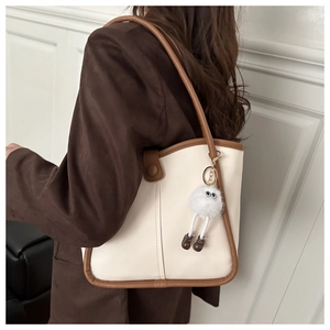 Detail of cream white tote bag with brown trim and cute plush doll pendant on shoulder
