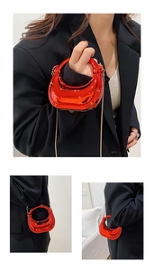 Polished red crescent evening bag with gold chain strap shown in detail and styled