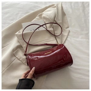 Close-up of wine red patent leather cylinder bag with gold fashion hardware and zipper