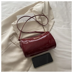 Détail du sac cylindrique en cuir verni bordeaux avec logo doré et bandoulière fine