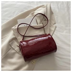 Detail of burgundy patent leather cylinder bag with glossy finish and gold-tone hardware