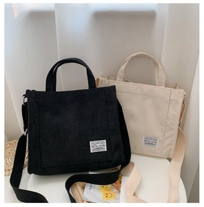 Detail of corduroy tote bags in black and beige with adjustable straps and retro label
