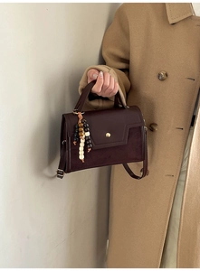Detail of vintage brown leather handbag with suede texture and beaded charm on coat