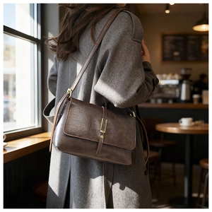 Brown vintage oil wax leather shoulder bag with metallic clasp worn in a cozy cafe setting