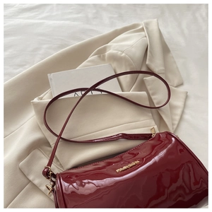 Detail of burgundy patent leather bag showing glossy texture and fashion metal logo