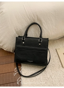 Detailed view of black lychee grain leather tote bag with silver hardware on a soft rug