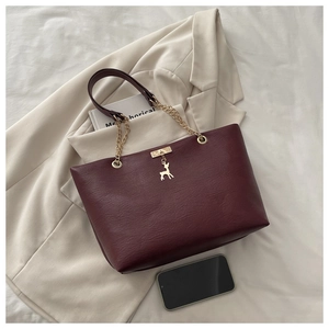Detailed close-up of wine red textured leather tote bag with golden deer charm detail