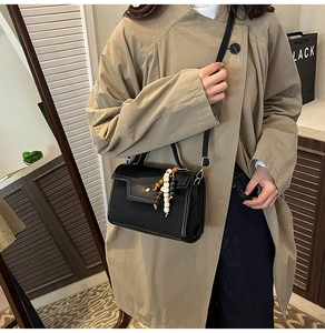 Detail of a black leather baguette bag with colorful beaded tassel on a khaki trench coat