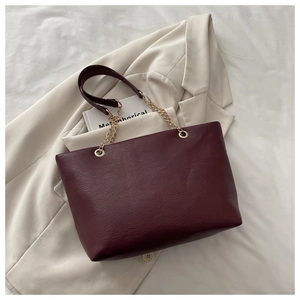 Détail d'un sac cabas bordeaux avec texture litchi et chaîne dorée sur blazer beige
