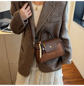 Détail d'un sac bandoulière en cuir marron avec rabat en daim et accessoire de perles